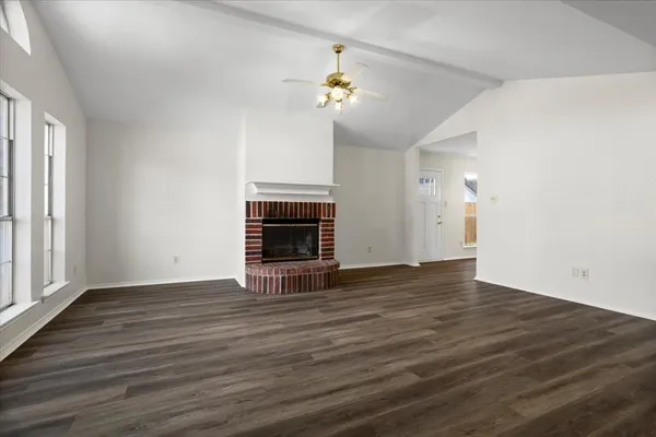 an empty room with wooden floor fireplace and windows