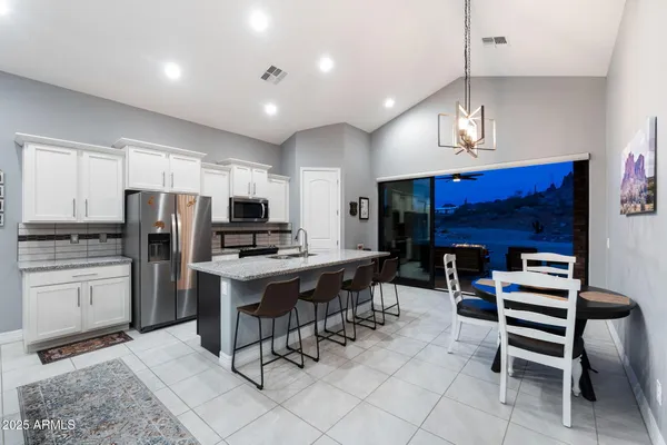 a kitchen with stainless steel appliances kitchen island granite countertop a refrigerator a stove a sink a dining table and chairs with wooden floor