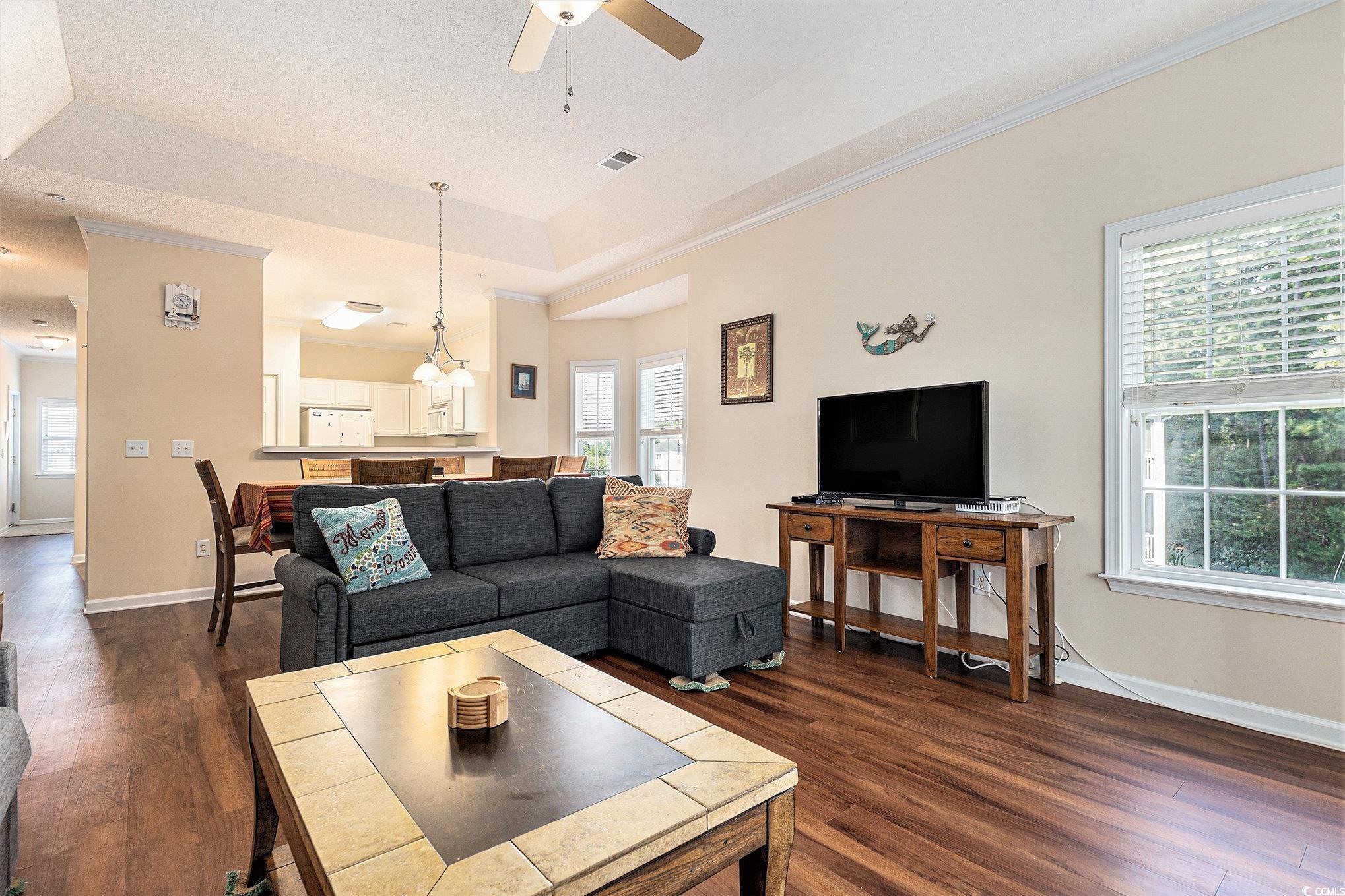 730 Charter Drive, Unit F11 Longs, SC 29568 - Photo 7 of 32 Living room with a raised ceiling, crown molding, dark wood finished floors, ceiling fan, and a chandelier