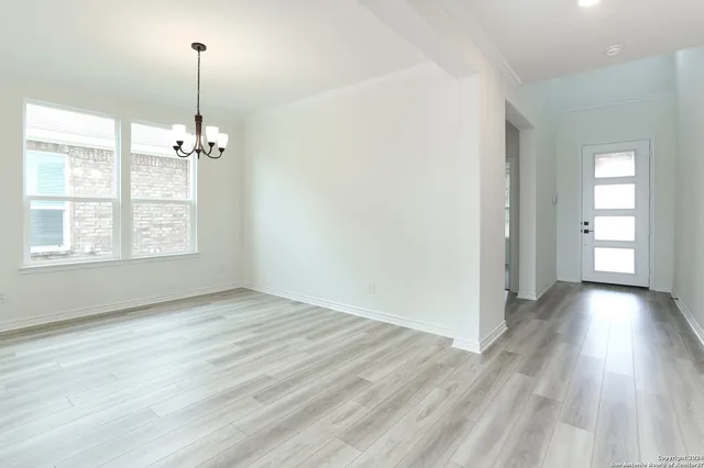 an empty room with wooden floor chandelier and windows