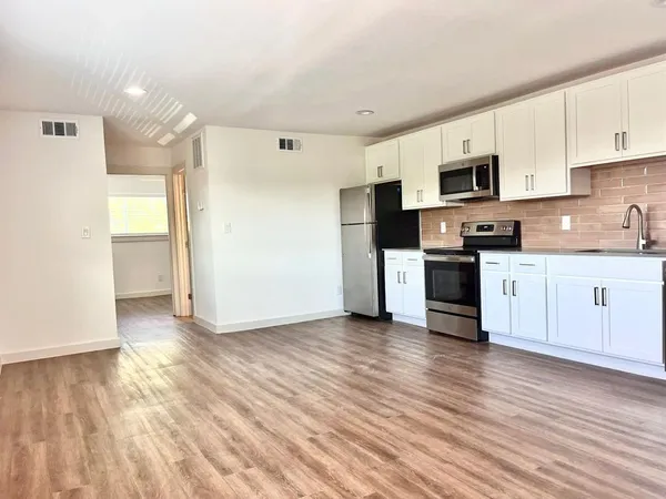 a kitchen with stainless steel appliances granite countertop a stove top oven a sink dishwasher and a refrigerator with wooden floor