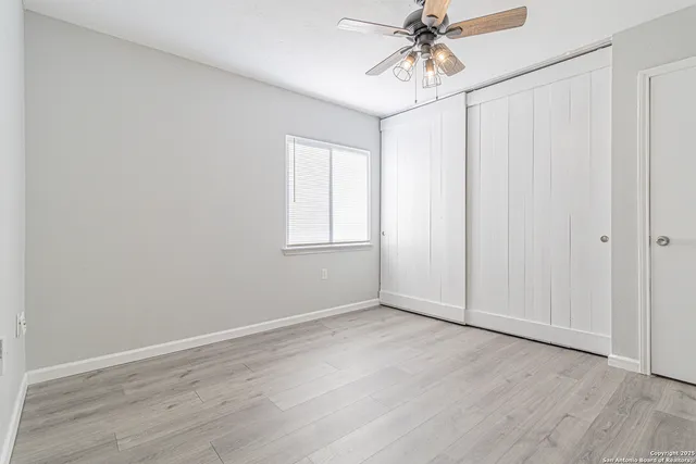 a view of an empty room with chandelier fan and wooden floor