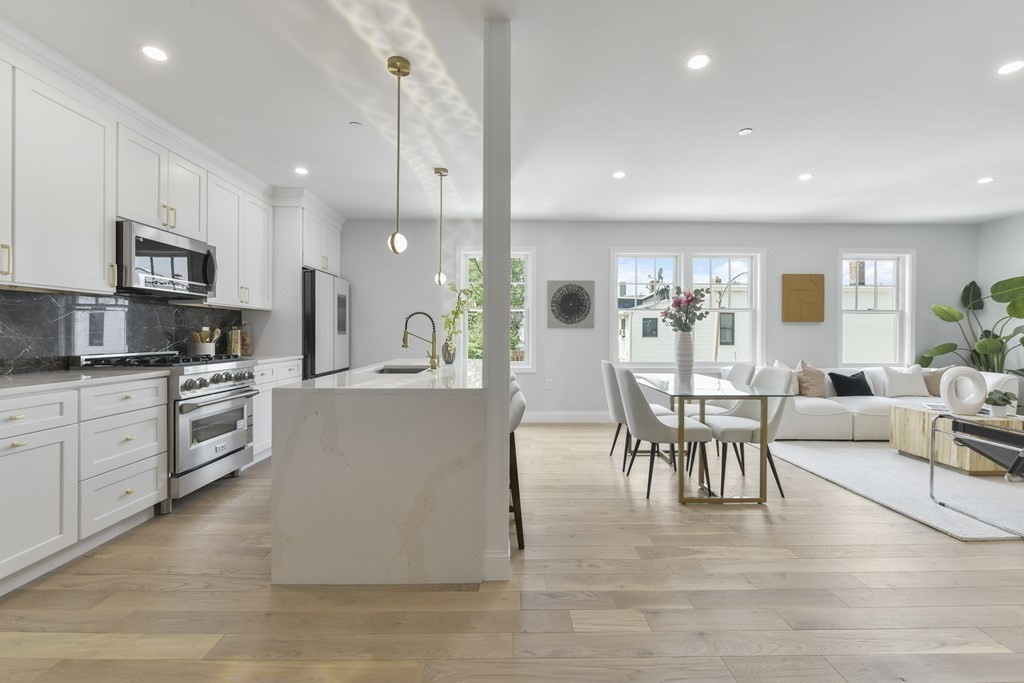 137 Falcon Street, Unit 4 Boston, MA 02128 - Photo 3 of 22 a large white kitchen with stainless steel appliances kitchen island granite countertop a stove a sink a dining table and chairs