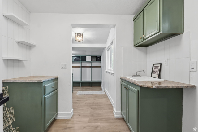 4270 River Road Oakley, UT 84055 - Photo 19 of 46 Kitchenette featuring sage green cabinetry, stone-look countertops, a built-in sink with faucet, white tiled backsplash, and wood-finish flooring