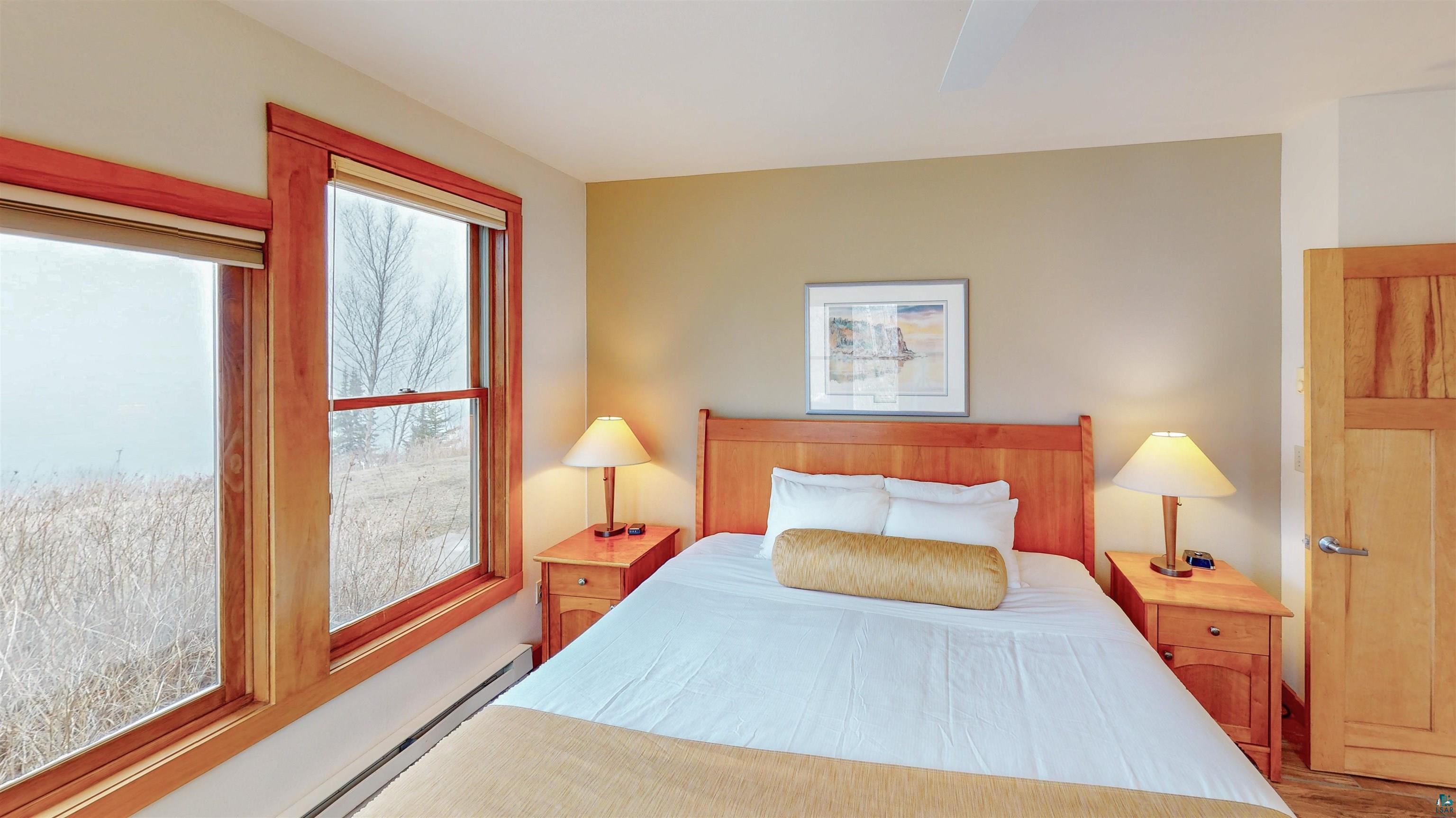 504-506 Poplar River Road, Unit 505 Lutsen, MN 55612 - Photo 13 of 39 Bedroom featuring expansive windows with wood trim, neutral wall tones, a ceiling fan, and a wood-finish door