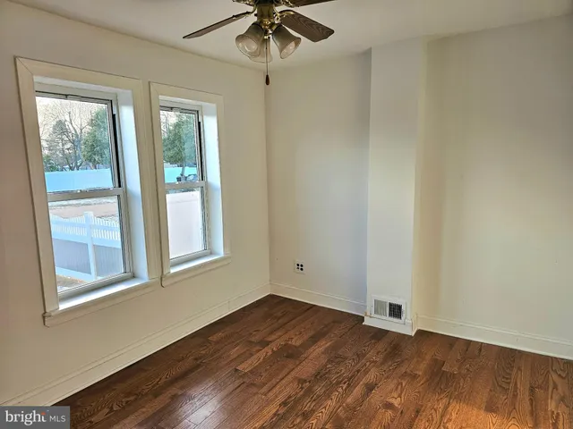 an empty room with wooden floor fan and windows