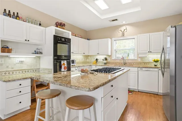 a kitchen with stainless steel appliances granite countertop a sink a stove a refrigerator and island with wooden floor