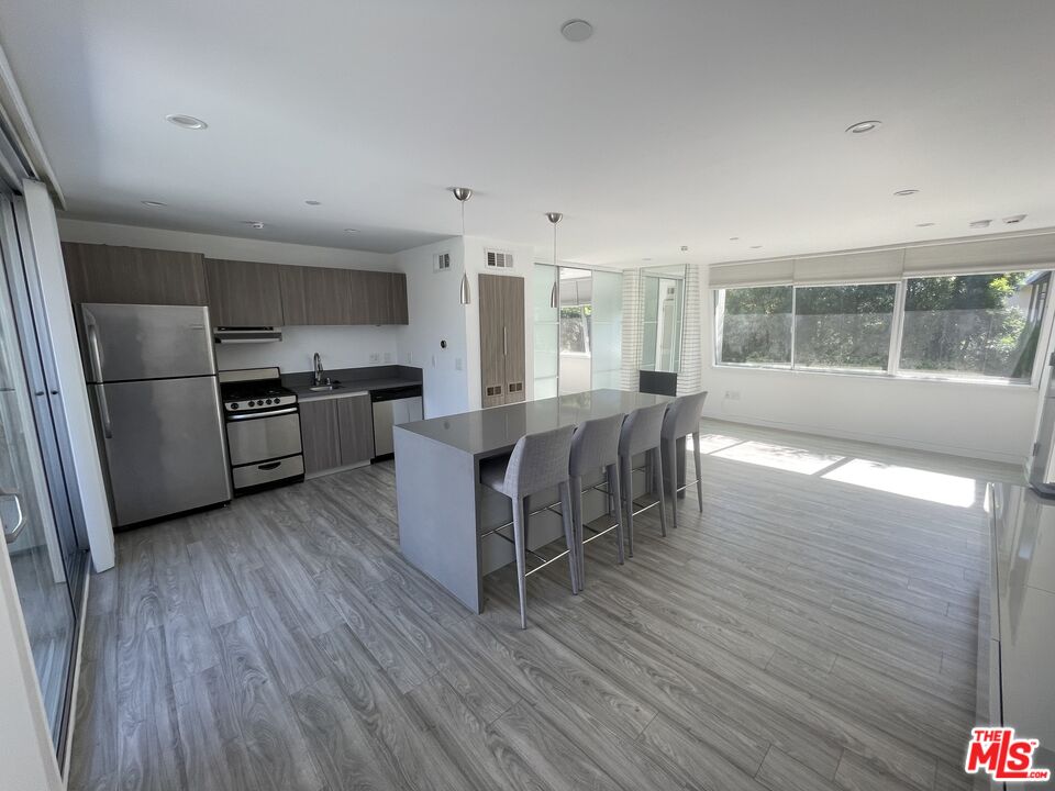a living room with stainless steel appliances granite countertop a stove a refrigerator a sink dishwasher a oven with wooden cabinets and wooden floor