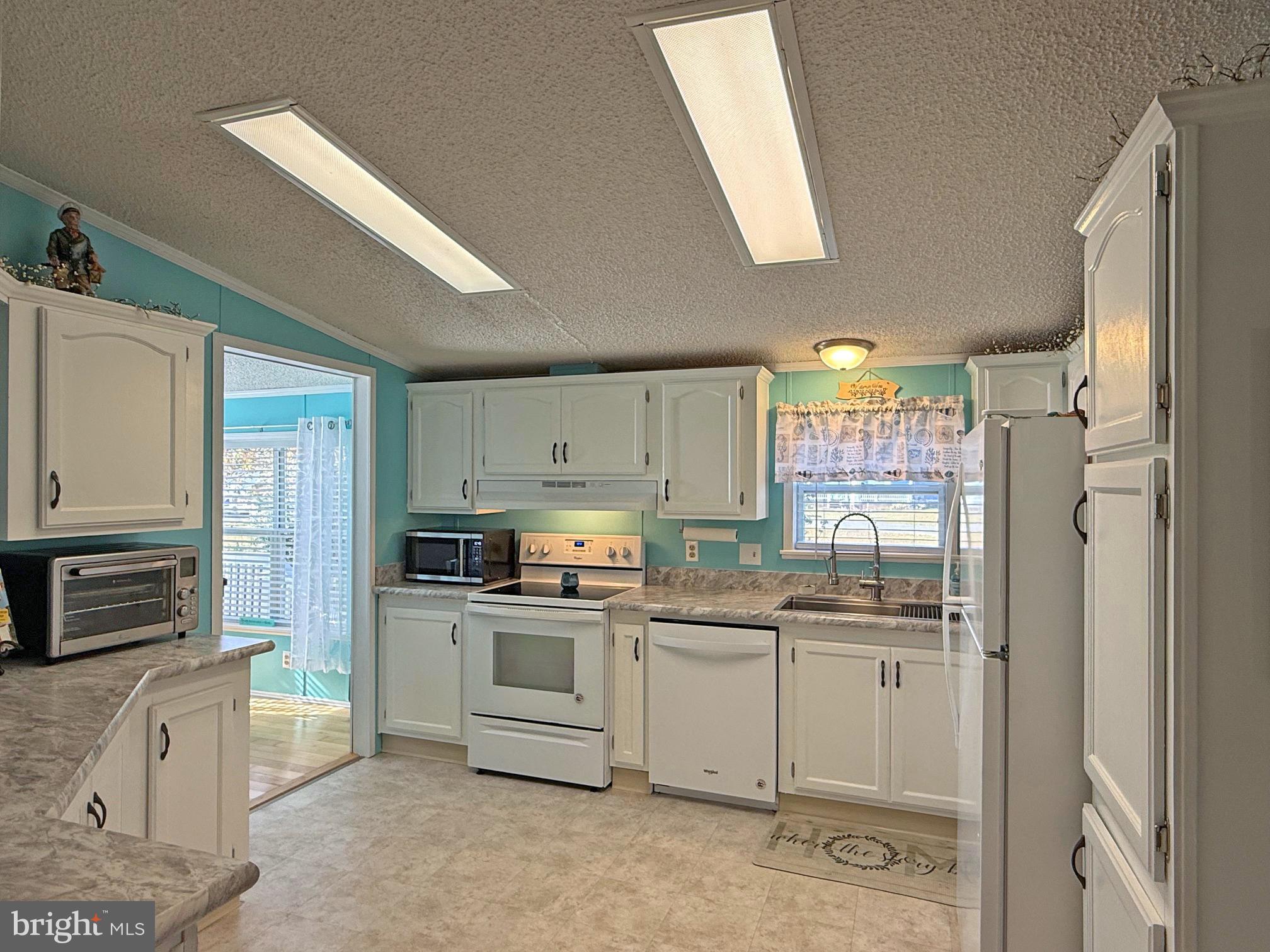 27137 Clipper Road, Unit M55 Millsboro, DE 19966 - Photo 7 of 48 a kitchen with stainless steel appliances granite countertop a stove top oven a sink a refrigerator and white cabinets
