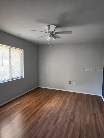 an empty room with wooden floor fan and windows