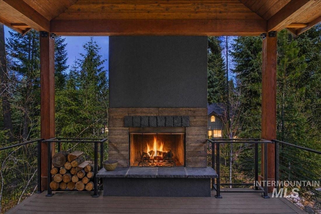 1051 Bitterroot Drive McCall, ID 83638 - Photo 2 of 26 Outdoor covered deck featuring a wood-burning fireplace with a stone hearth and wood-planked surround, exposed timber beams, and cable railings