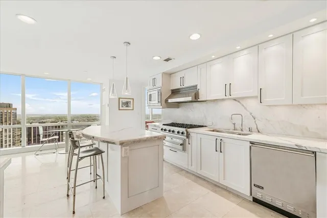 a kitchen with stainless steel appliances granite countertop a stove a sink and white cabinets with wooden floor
