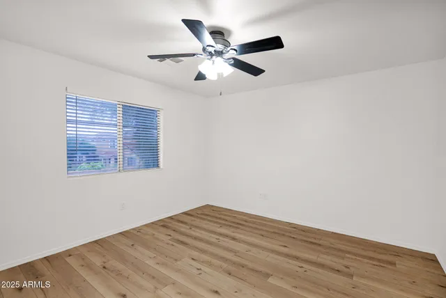 a view of an empty room with wooden floor and a ceiling fan