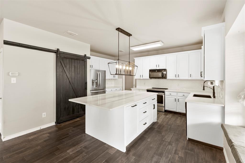 6522 Portside Ridge Lane Dallas, TX 75249 - Photo 10 of 37 Kitchen featuring a central island with a solid surface countertop, white cabinetry with black hardware, wood-finish flooring, a stainless steel refrigerator, and a dark wood barn door