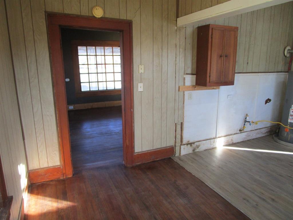 1206 South Main Street Quanah, TX 79252 - Photo 20 of 22 Spare room with dark wood-type flooring, gas water heater, and wood walls