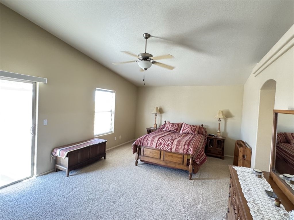 3316 Producers Mine Road Kingman, AZ 86401 - Photo 25 of 35 Spacious bedroom featuring a vaulted ceiling with a ceiling fan, light-colored carpeting, a large sliding glass door, an additional window with blinds, and an arched entryway