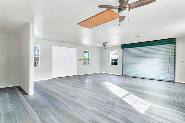 an empty room with wooden floor ceiling fan and windows