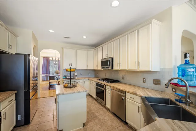 a kitchen with stainless steel appliances granite countertop a sink dishwasher a refrigerator oven and white cabinets next to a window