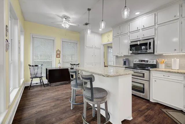 a kitchen with stainless steel appliances granite countertop a stove top oven a sink a dining table and chairs with wooden floor