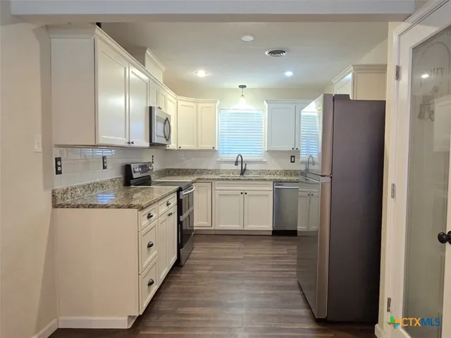 a kitchen with stainless steel appliances granite countertop a sink cabinets and wooden floor