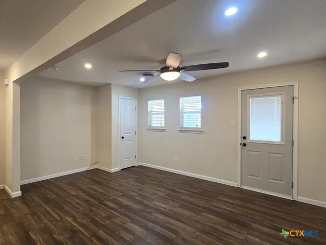 a view of an empty room with wooden floor and a ceiling fan