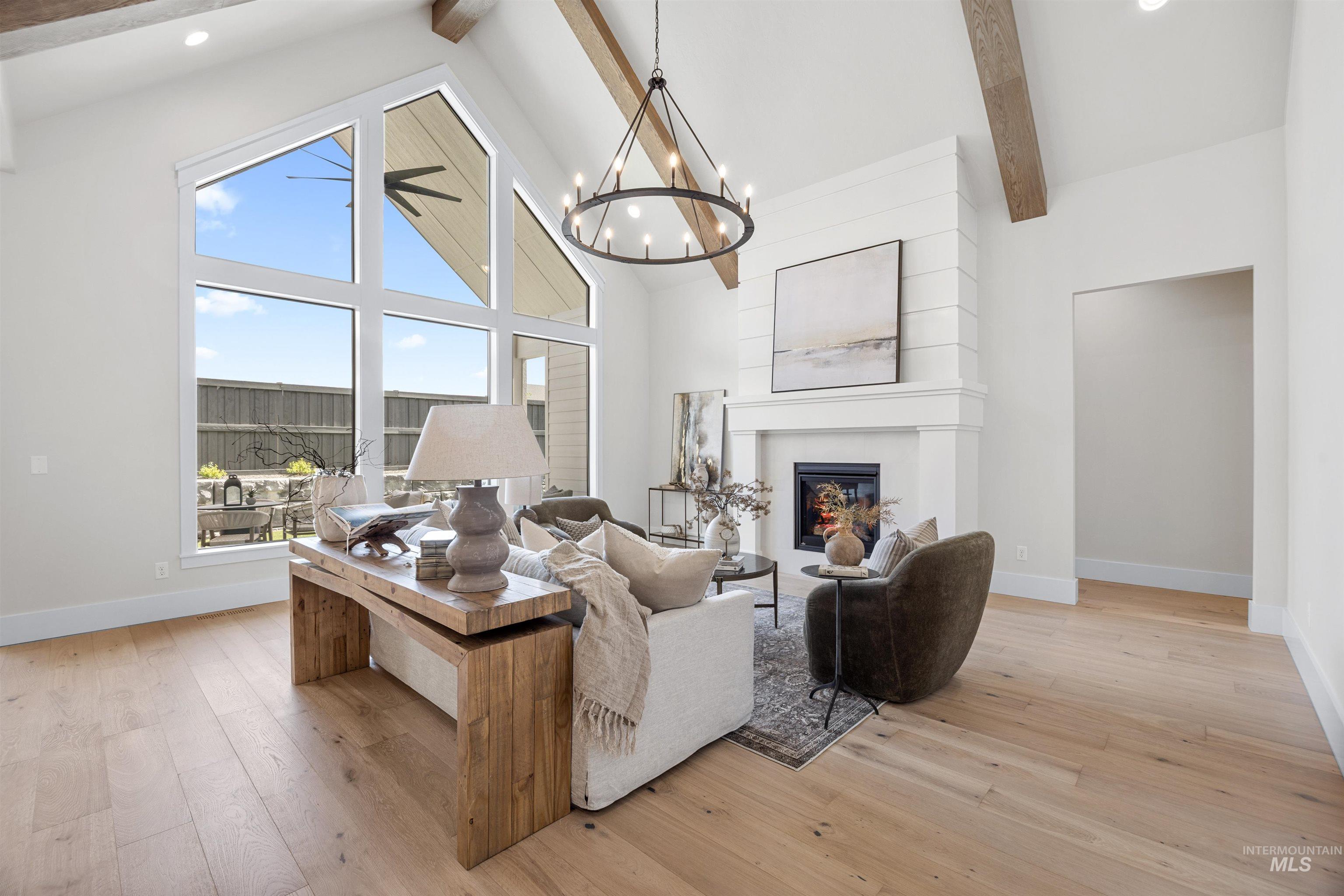 5940 South Pinpoint Way Meridian, ID 83642 - Photo 11 of 40 Vaulted ceiling with exposed wood beams, expansive window wall, light wood-finish flooring, built-in fireplace, and a large chandelier