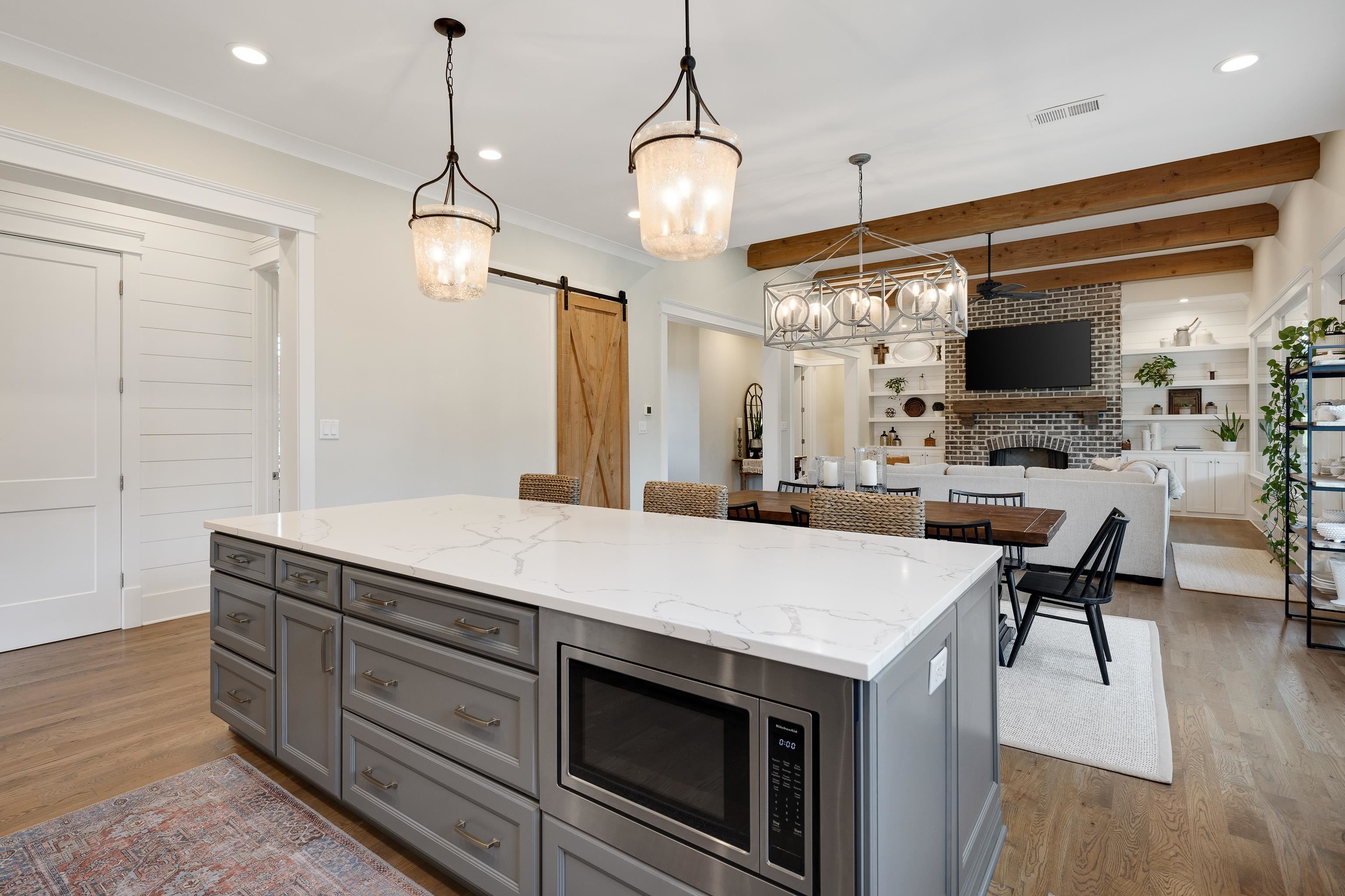 805 Shady Grove Road Williston, TN 38076 - Photo 16 of 40 Kitchen island with a white countertop and integrated microwave, decorative pendant lighting, wood-finish flooring, exposed ceiling beams, and a brick fireplace