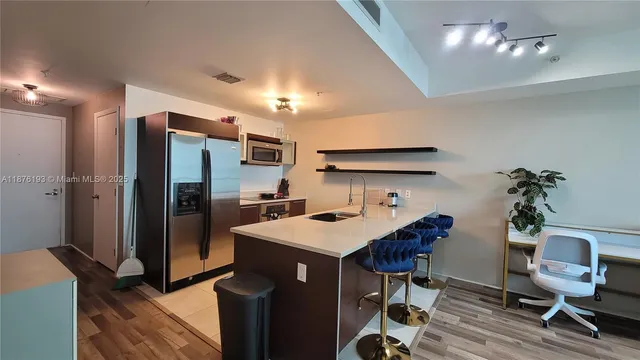 a kitchen with stainless steel appliances a sink dishwasher a refrigerator and a dining table with wooden floor