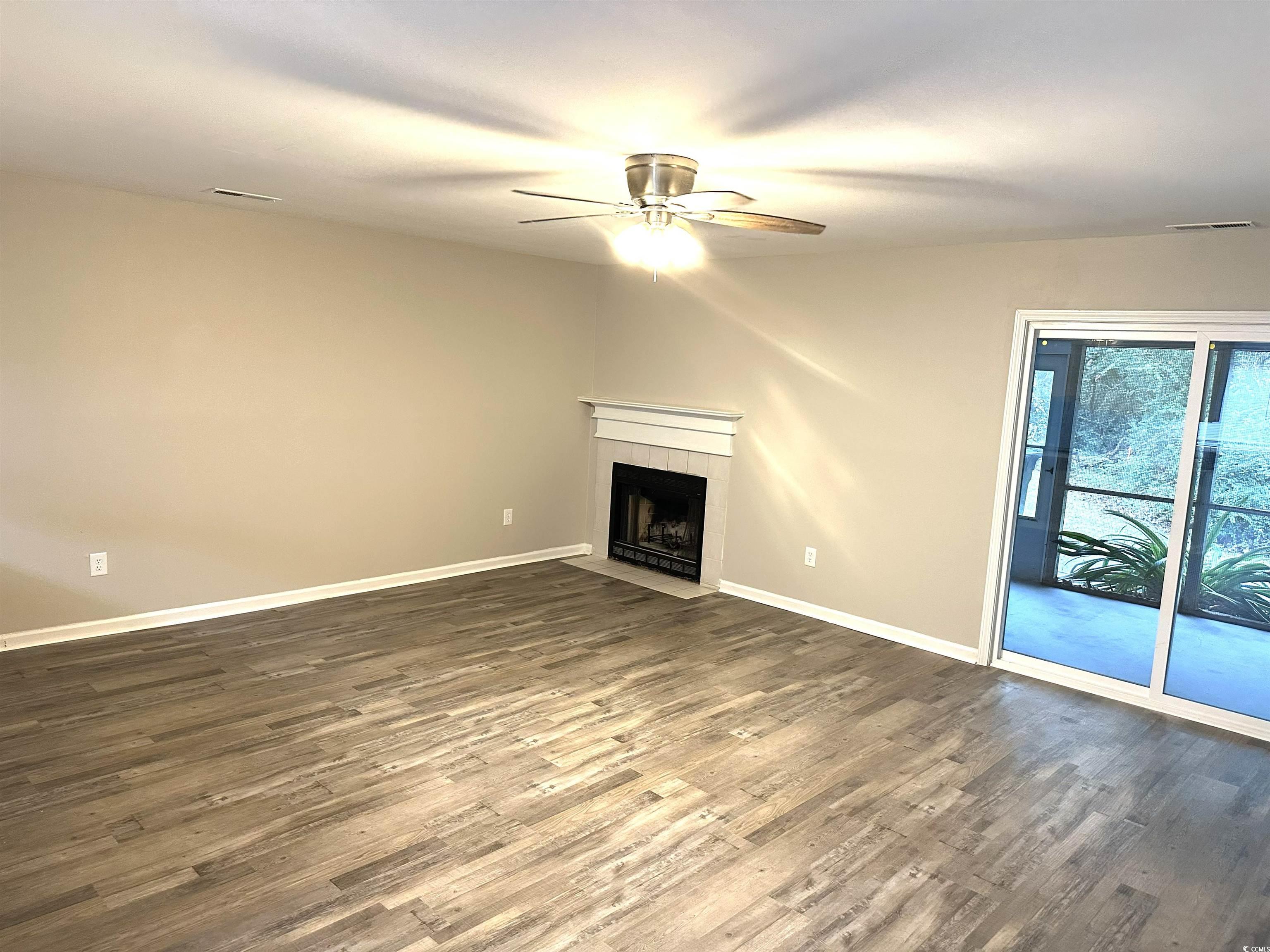 178 Beaver Pond Loop, Unit 60 Pawleys Island, SC 29585 - Photo 3 of 21 Unfurnished living room with dark wood-style floors, a ceiling fan, and a tiled fireplace