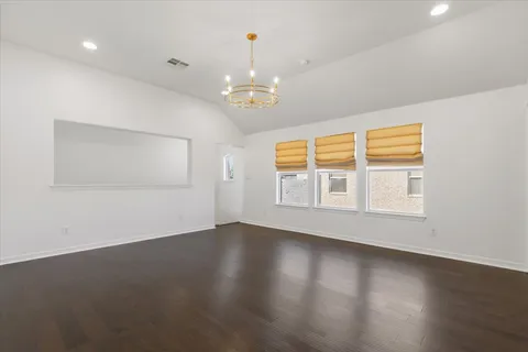 an empty room with wooden floor chandelier and windows