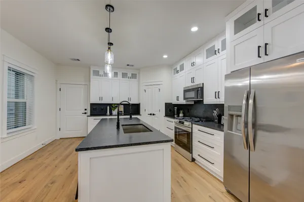 a kitchen with granite countertop a refrigerator a stove a sink dishwasher and white cabinets with wooden floor