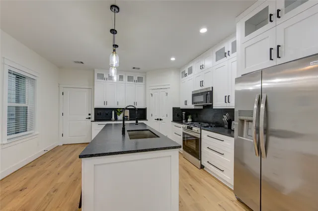 a kitchen with granite countertop a refrigerator a stove a sink dishwasher and white cabinets with wooden floor