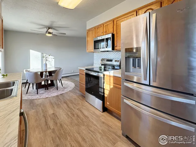 a kitchen with stainless steel appliances granite countertop a refrigerator a stove top oven a dining table and chairs with wooden floor