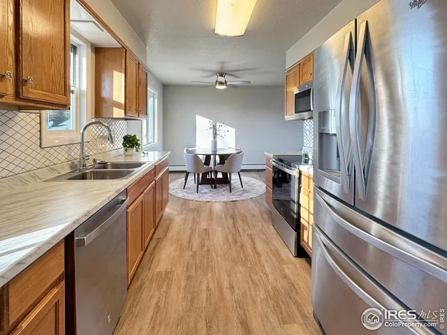 a kitchen with stainless steel appliances granite countertop a refrigerator a sink dishwasher a stove and white countertops with wooden floor