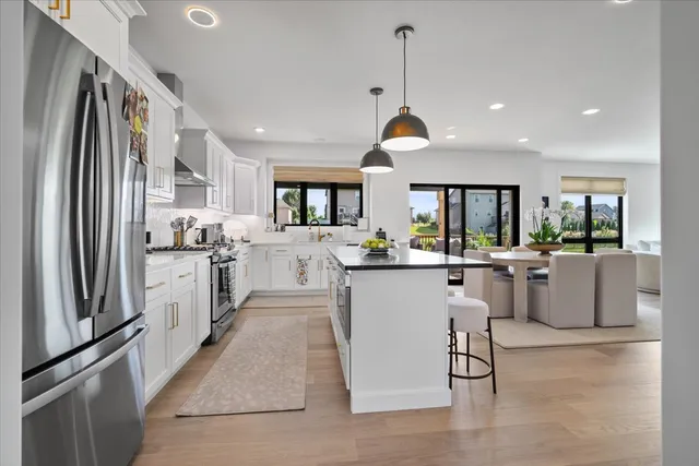 a kitchen with stainless steel appliances kitchen island granite countertop a refrigerator a stove a sink dishwasher and white cabinets with wooden floor