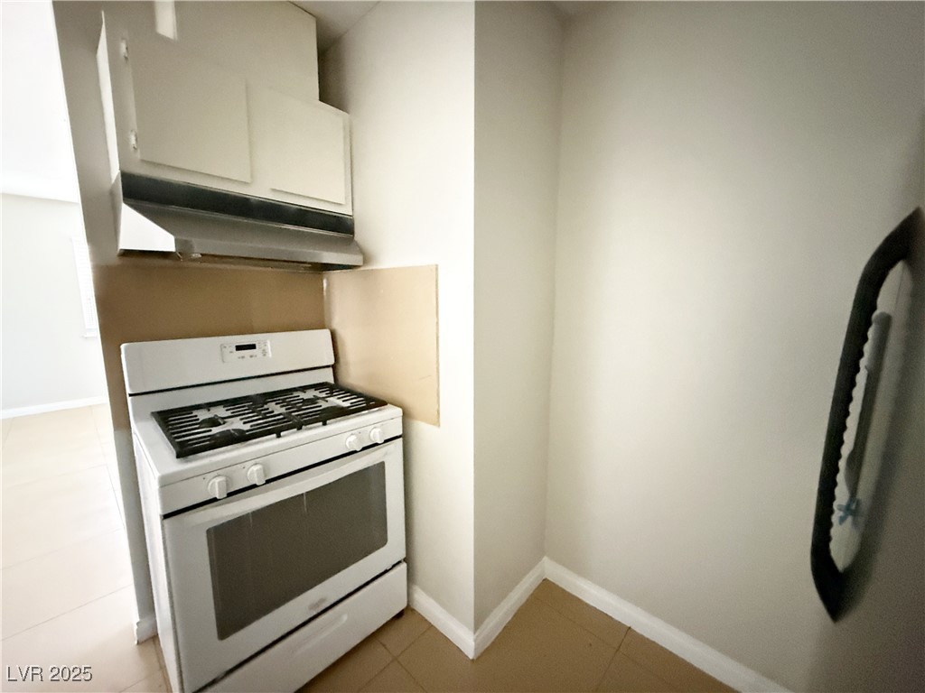 2353 Exeter Drive, Unit B Las Vegas, NV 89156 - Photo 10 of 16 Kitchen featuring white gas stove, light tile patterned floors, under cabinet range hood, and white cabinets