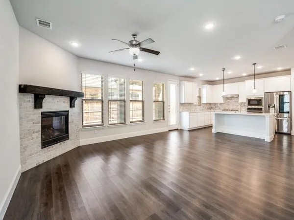 a view of an empty room with wooden floor and a kitchen
