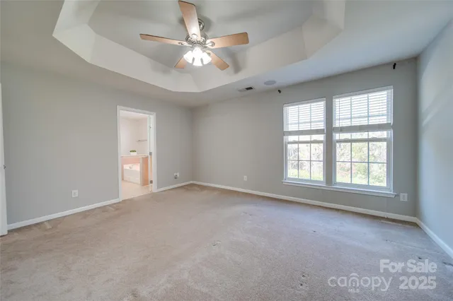 an empty room with chandelier fan and windows