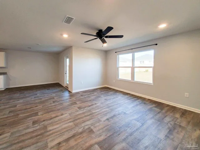 an empty room with wooden floor ceiling fan and windows