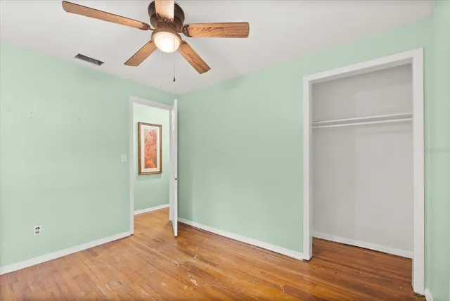 an empty room with wooden floor closet and ceiling fan