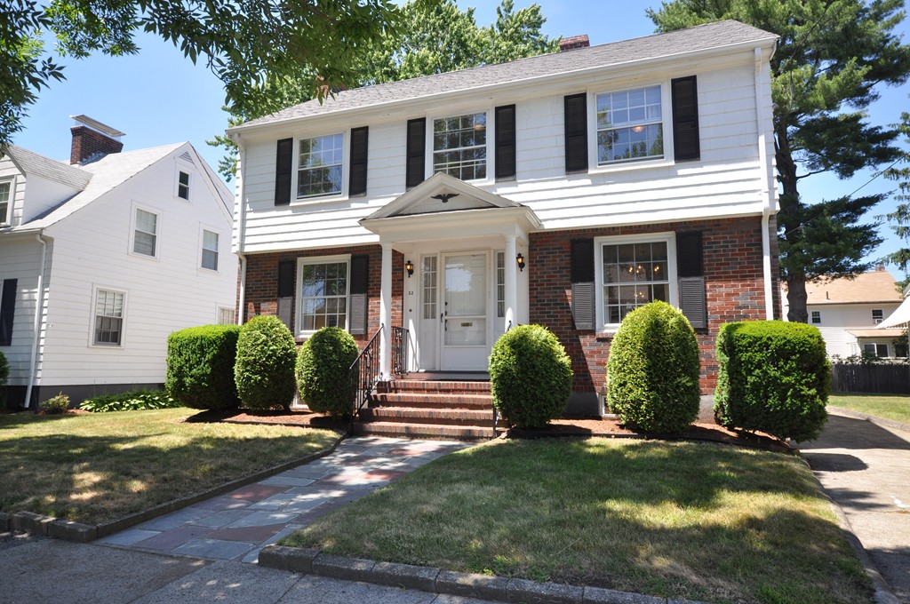 a view of a white house with a yard plants and large tree