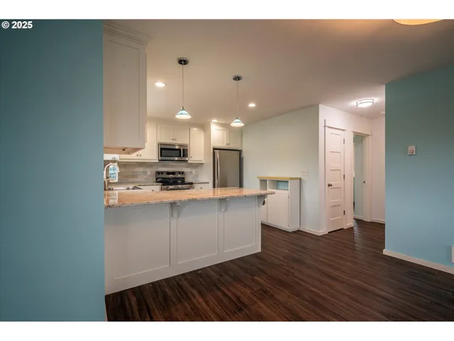 a open kitchen with kitchen island white cabinets wooden floor and stainless steel appliances