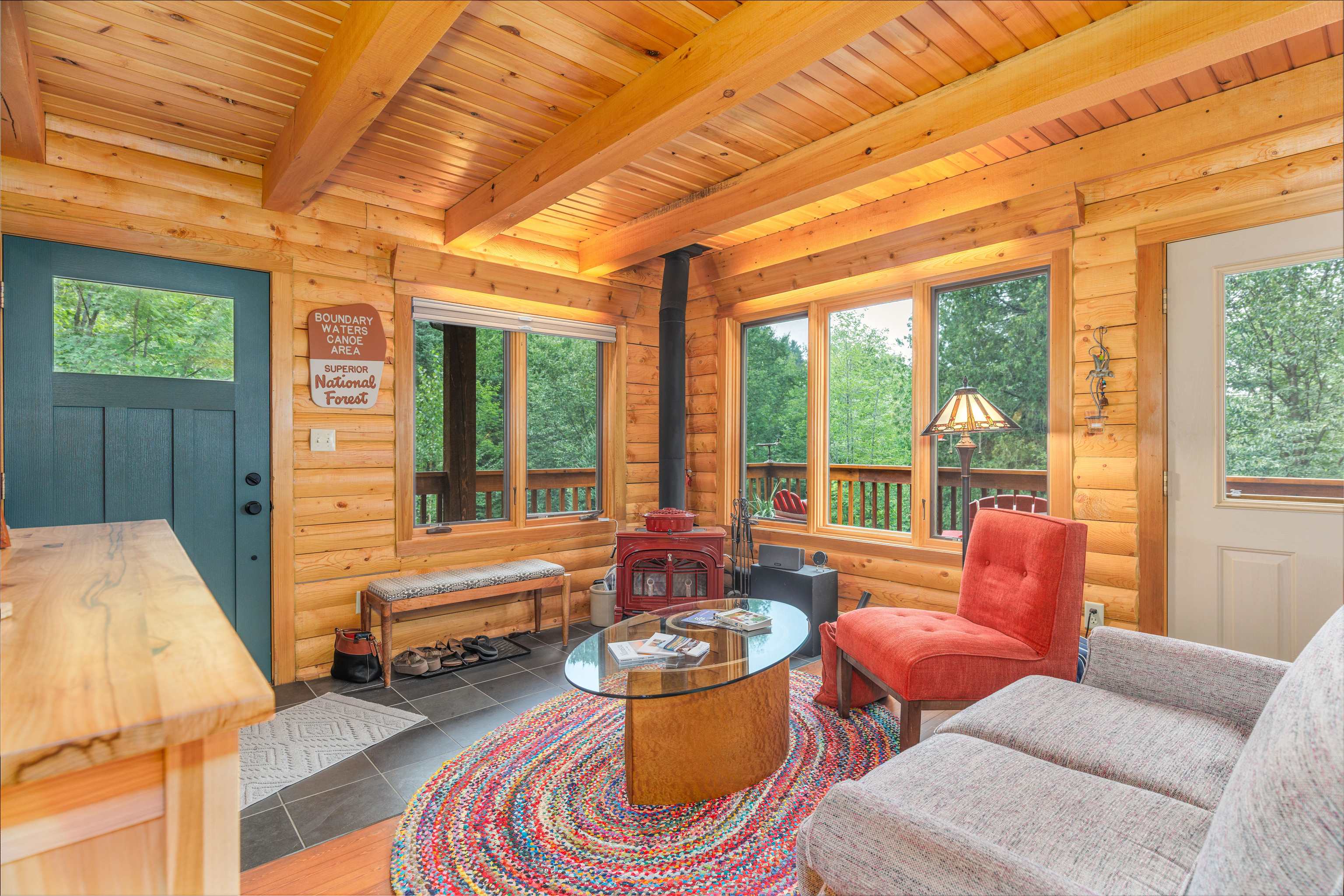 540 Loop Road Ely, MN 55731 - Photo 3 of 20 Living area featuring a wood stove, a wooden ceiling with exposed beams, rustic walls, plenty of natural light, and tile patterned floors