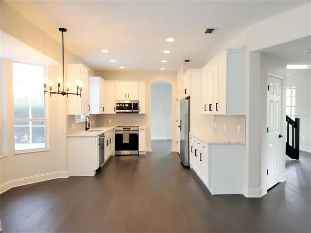 a kitchen with stainless steel appliances kitchen island granite countertop a refrigerator a oven a sink and white cabinets with wooden floor