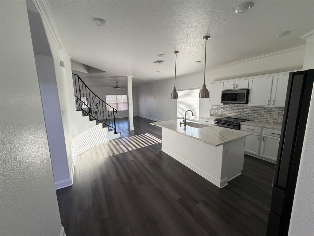 8045 Ballater Drive Fort Worth, TX 76123 - Photo 13 of 26 Kitchen featuring white cabinetry, an island with sink, hanging light fixtures, appliances with stainless steel finishes, and a textured ceiling