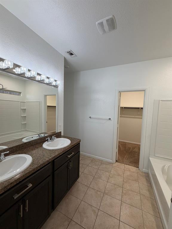8045 Ballater Drive Fort Worth, TX 76123 - Photo 25 of 26 Bathroom with a walk in closet, double vanity, a textured ceiling, light tile patterned flooring, and tub / shower combination