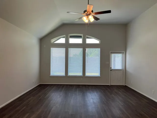 an empty room with wooden floor fan and windows