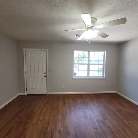an empty room with wooden floor chandelier fan and windows