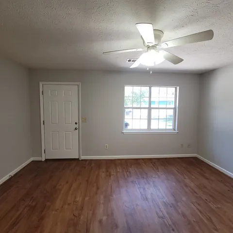 an empty room with wooden floor chandelier fan and windows