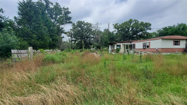 a backyard of a house with plants and large trees with wooden fence